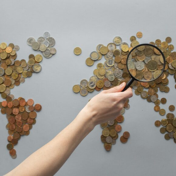 anonymous person magnifying view of coins shaped in world map