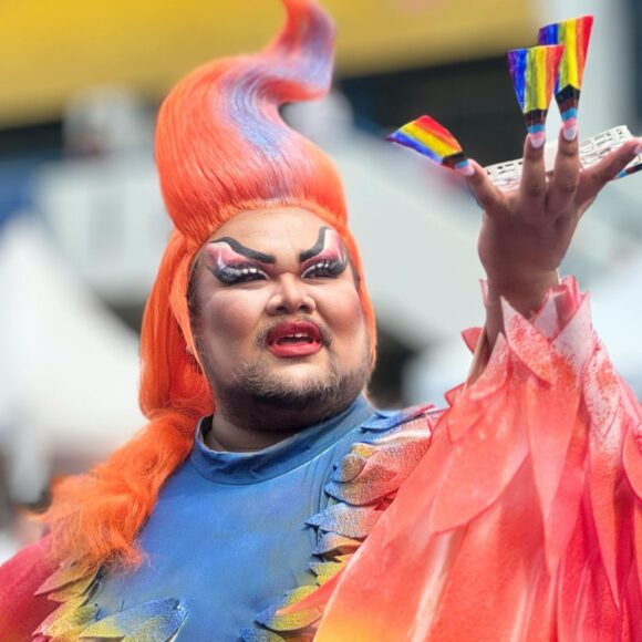 person in costume with progress pride flags on press on nails holding a drone
