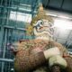 Colorful guardian demon statue indoors, hands folded around a staff, with an ornate headdress and patterned armor.